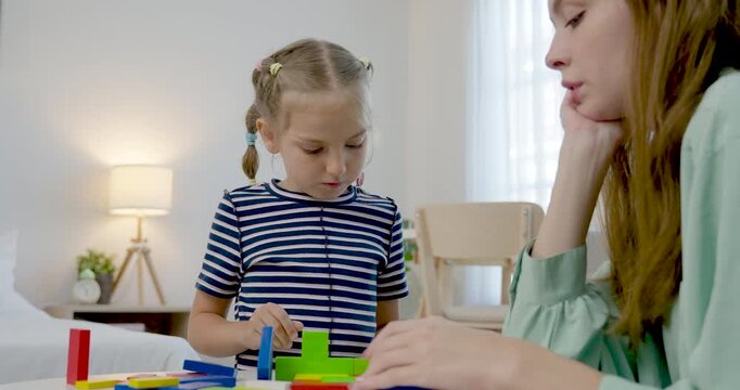 Close view of caucasian single mother coaching preschool daughter as child stacks colorful blocks, learns shape, balance, counting, creative play, patient parenting, home education routine indoors.