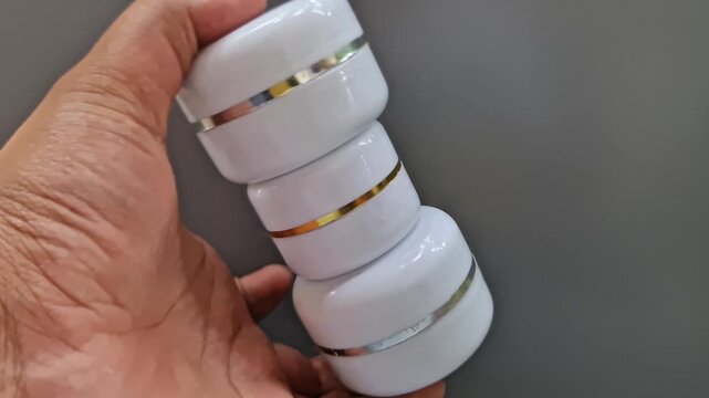 Sidoarjo, Indonesia - 24 May, 2026: Hand Holding Open Dermatology Cream Jar on Gray Background, Clinical Skincare Moisturizer Container for Medical and Beauty Treatment