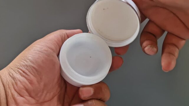 Sidoarjo, Indonesia - 24 May, 2026: Hand Holding Open Dermatology Cream Jar on Gray Background, Clinical Skincare Moisturizer Container for Medical and Beauty Treatment