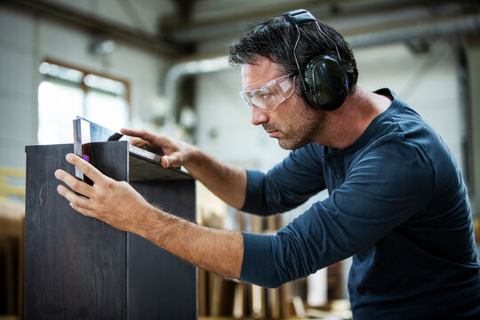 Man measuring out and examining the cabinet he is building.