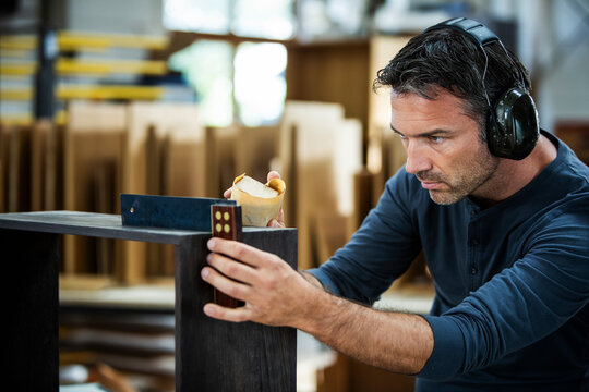 Man measuring out and examining the cabinet he is building.