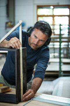 Man measuring out and examining the cabinet he is building.