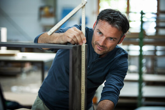 Man measuring out and examining the cabinet he is building.