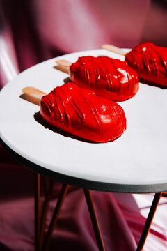 Glossy red cakesicles arranged on a bright white table against a soft pink fabric