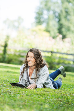 Young happy woman sitting in grass and using an ipad. 