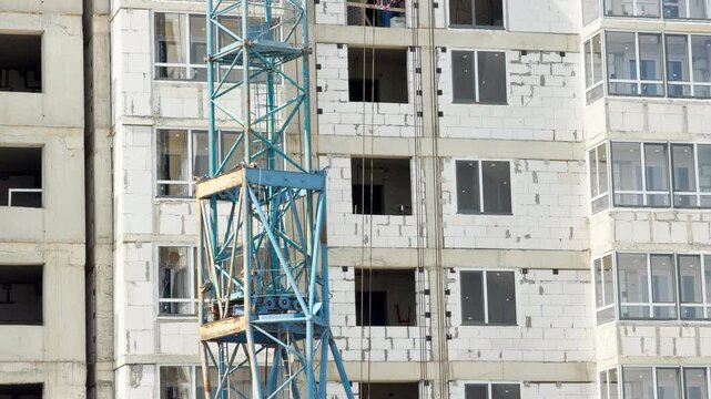 A blue metal crane stands before an unfinished concrete building. Heavy machinery runs actively across the site. The busy development creates a continuous low mechanical hum.