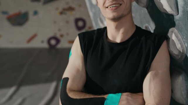 Portrait of young man with kinesiology tape on arm smiling at camera in climbing gym, tilt up shot. Clip is ideal for sports medicine, active lifestyle, and physical therapy ads