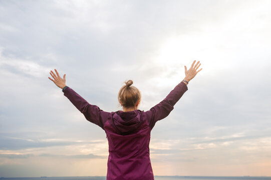 Coastal woman rises hands beneath dramatic clouds and sea