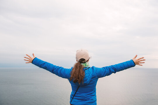 Freedom woman rises hands beneath dramatic clouds and sea