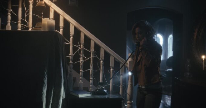 Nervous, lone, young woman picking up rotary phone in scary, dark home - tracking wide shot