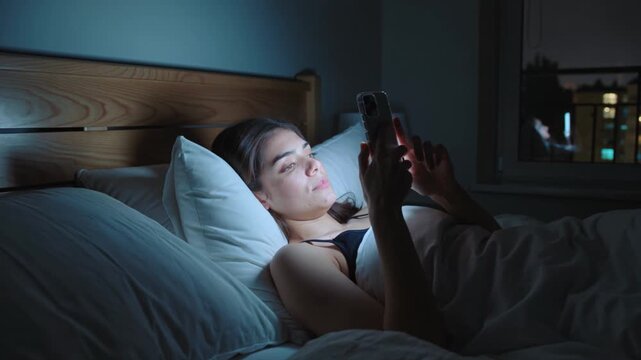 Smartphone, woman and bed at night for social media, scrolling and internet browsing. Female, mobile phone and screen light in bedroom with insomnia, technology and dark home apartment life news