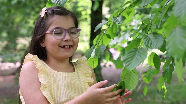 A joyful compilation video featuring a cute little girl with purple glasses and a yellow summer dress enjoying a sunny spring day in the park. The footage captures her posing by blooming white spirea 