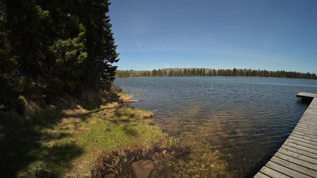 Wide angle view of a small northern lake and wooden dock under a blue sky with small waves on the water
