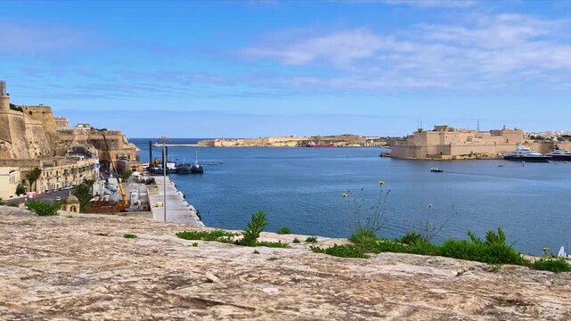 View across the Grand Harbor towards Fort St Angelo and historic fortifications under blue sky in Valletta