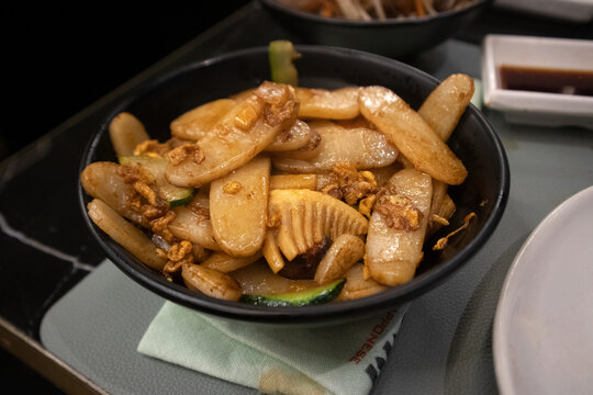 Gnocchi di riso cinesi saltati nel wok con germogli di bamb&ugrave;, verdure e salsa di soia serviti caldi in una ciotola nera da ristorante asiatico