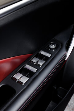 Vertical view of modern car door armrest with power window switches and side mirror control knob. Luxury vehicle black and red leather interior armrest trim with silver buttons, nobody