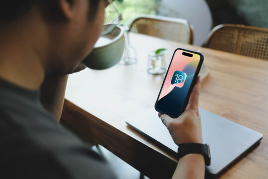 Bangkok, Thailand. May 27, 2026; A person holding a smartphone displays the Apple iOS 18 operating system logo while drinking coffee in a cafe.