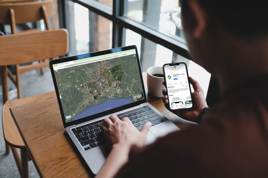 Bangkok, Thailand. May 29, 2026; An over the shoulder view of a person using a laptop and a smartphone to access Google Maps for navigation and transit information.