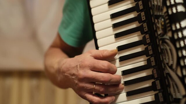 A musician plays an accordion and demonstrates various finger movements. The setting is a cozy home in the evening time.