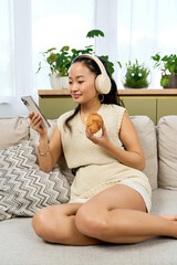 Obraz premium Young woman enjoys a cozy afternoon with music and a snack in her modern apartment