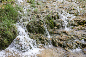 Fototapeta premium Small waterfalls flowing over rocky terrain. Natural cascade landscape in forest environment. Fresh river stream background. Scenic national park attraction outdoors. Water movement and nature detail.