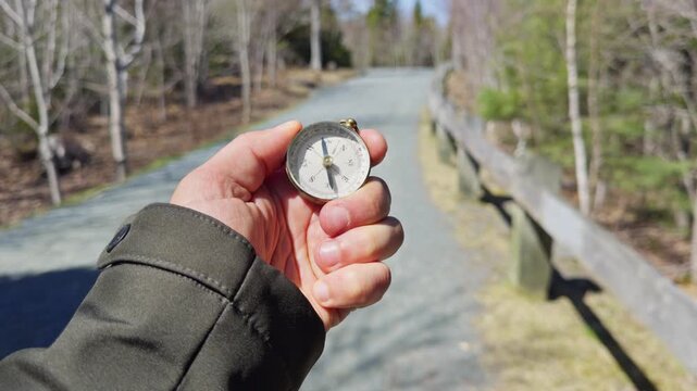 Experiencing the great outdoors while holding a compass, the human hand guides the way. Surrounded by beautiful trees, the path stretches into the serene landscape, inviting adventure