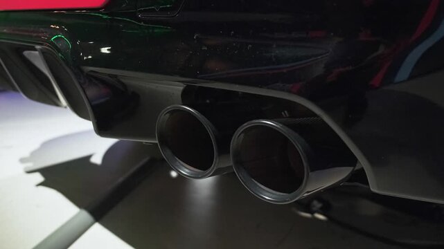 Close-up cinematic footage of sporty quad exhaust pipes on a modern luxury performance sedan, highlighted by dramatic showroom lighting and premium automotive styling.