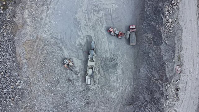 Multiple trucks and machinery work together at a mining site. Workers monitor the process as materials are extracted from the ground and moved for further use. Dust rises around the equipment.