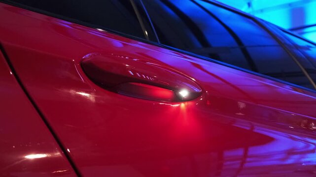 Close-up of red high-performance sports sedan door handle recess with soft spotlight reflection on glossy metallic bodywork. Premium luxury performance car exterior detail for automotive editorial con