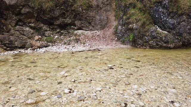 Clear flowing river water in a mountain stream with stones, rocky shoreline and cliff landscape in pristine alpine nature