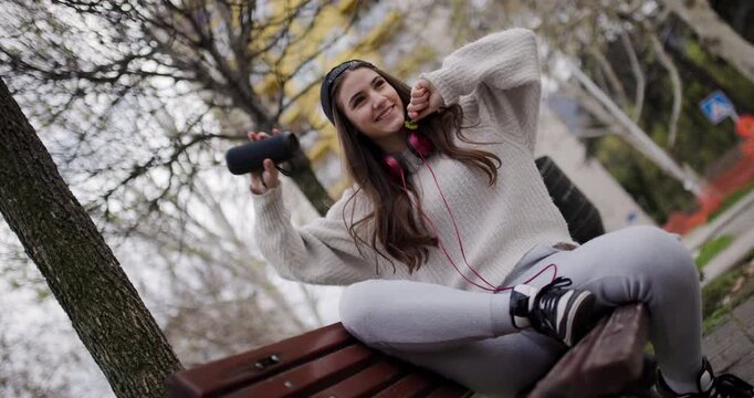 Carefree Teen Girl Enjoys Music on Headphones and Dances with a Bluetooth Speaker in a Park - Slow Motion Low Angle