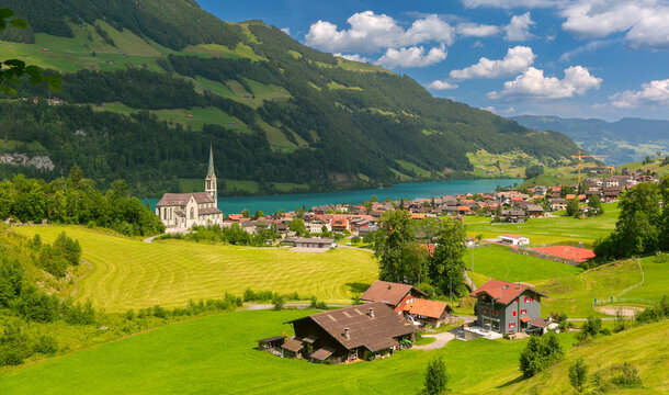 Traditional Swiss village with church buildings located near turquoise Lungern lake and green alpine slopes.