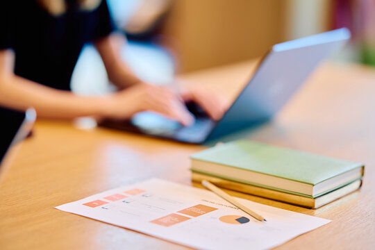 Woman's hands typing on a laptop keyboard, focusing on work at a desk with financial charts and study materials