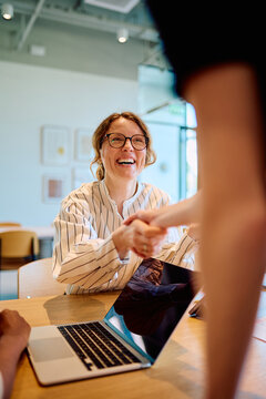Woman in glasses shaking hands with unseen person, celebrating a successful business deal, partnership, or collaboration in an office