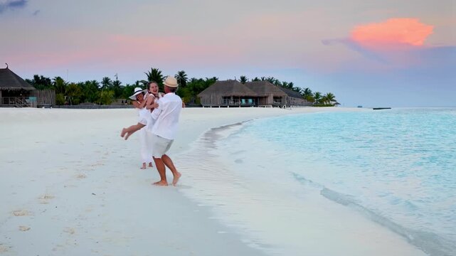 A happy holiday family is having fun on a tropical beach in the Maldives islands during sunset time