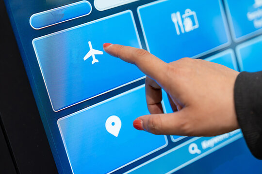 Asian woman touching the screen of an automatic airline ticket vending machine.