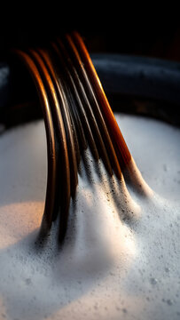 A close-up, dramatically lit image shows several dark, curved, parallel tubes emerging into a basin filled with thick white soap suds.
