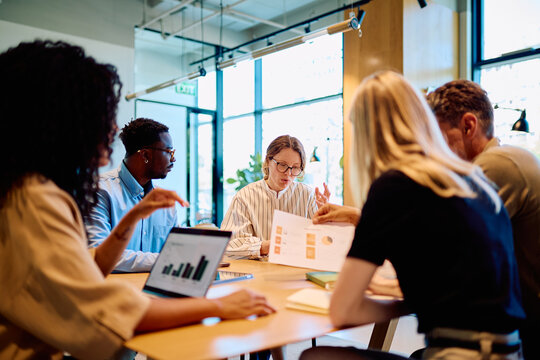 Diverse business professionals collaborating on a project, analyzing data, and brainstorming ideas during a corporate meeting in a modern office