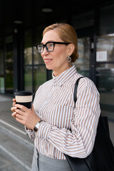 Fototapeta premium Elegant woman enjoying coffee outdoors while wearing stylish glasses and a striped shirt