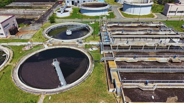 Close aerial view of circular clarifiers showing rotating scrapers, dark sludge pools, parallel aeration channels, concrete platforms, maintenance access