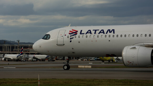 Jato comercial da LATAM taxiando em Guarulhos, com pista, &aacute;rea gramada e nuvens densas compondo o cen&aacute;rio aeroportu&aacute;rio. Guarulhos, SP, 10 de maio de 2026.
