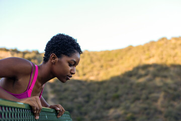 Obraz premium Person in a pink top leans over a railing, overlooking a scenic view.