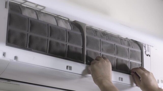 Removing a dusty air filter from a wall-mounted air conditioner for cleaning. Concept of DIY appliance maintenance and dust allergy prevention.