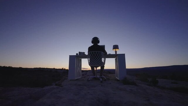 Silhouette of Person Working at Computer Desk in Desert During Blue Hour