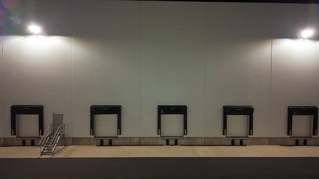 The video shows loading docks in an industrial area at night. The lights shine on the large white wall. The docks are empty with no vehicles present