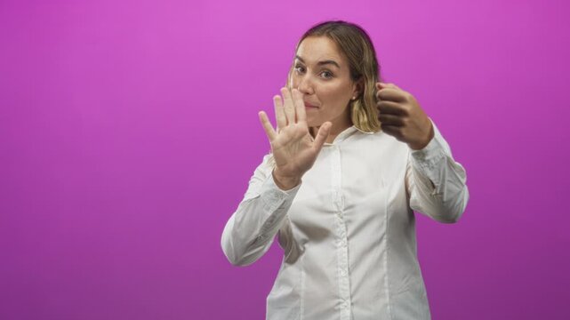 Woman blonde in white shirt miming steering wheel with both fists forward and raising an open palm in studio; assertive pause.