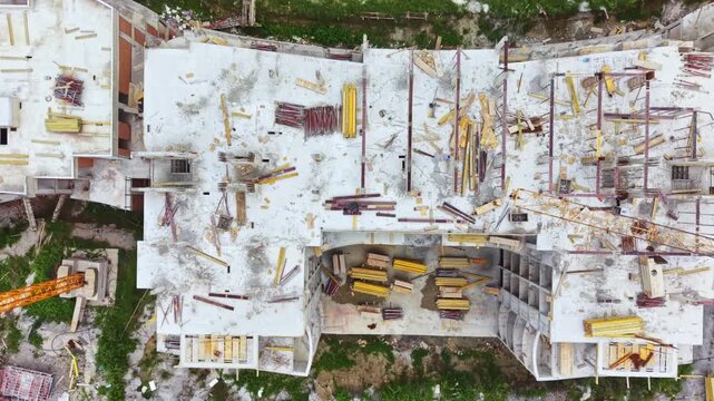 Topdown view concrete slab construction site with central courtyard of yellow excavators and loaders, dense rebar grids and formwork crane lifting panels, crews