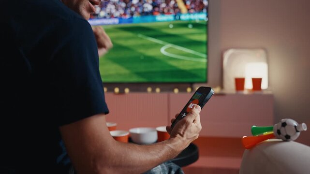 Excited soccer fan placing bet on smartphone and celebrating goal