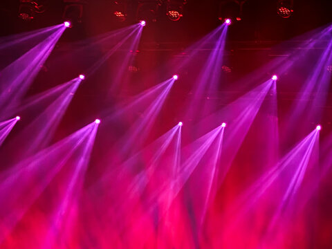 abstract background of stage beams and lights in pink, red and purple during live concert
