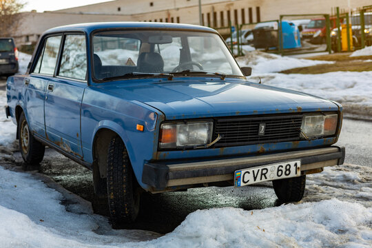 Vilnius, Lithuania - March 2 2026: Front view of classic blue Lada 2105 Soviet sedan parked on snowy winter street. Rust details on vintage body, frozen slush and wet asphalt after thaw.